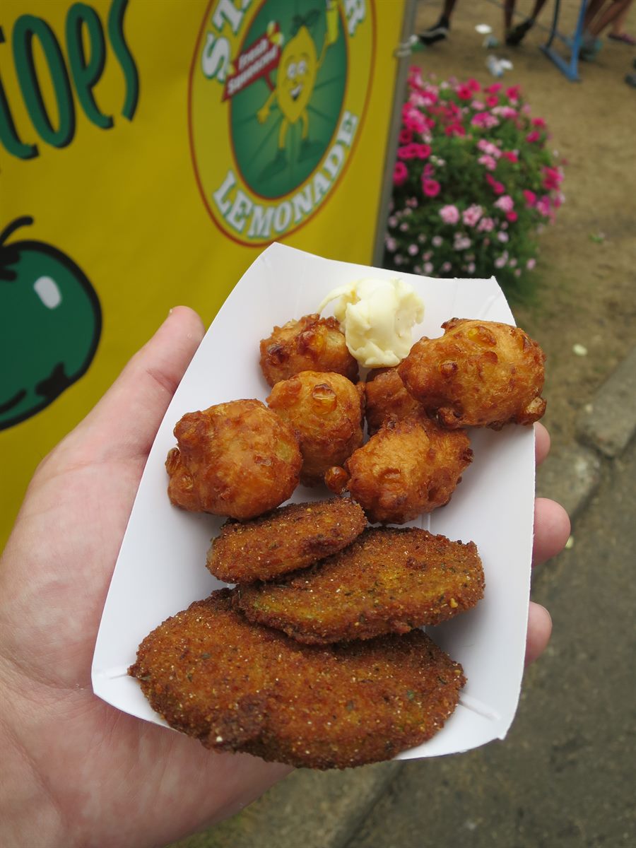 Tray of fritters and fried green tomatoes in front of a yellow lemonade banner with a green tomato painted on it