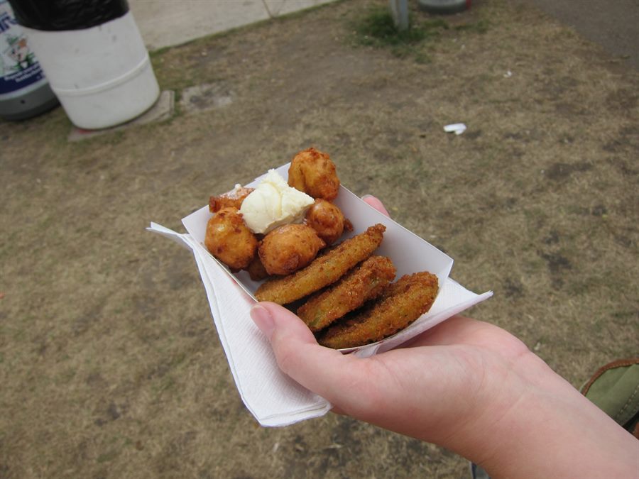 White paper tray of corn fritters, butter, and fried green tomatoes held in one hand